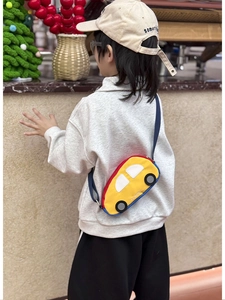 Detail showing the cartoon car crossbody bag worn by a child in a home setting