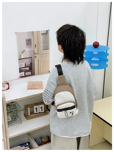 Vue arrière d'un sac bandoulière bicolore beige et blanc porté par un jeune modèle