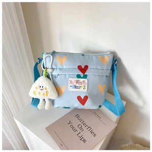 Détail du sac à bandoulière en toile bleu clair avec motifs de cœur et pendentif en peluche
