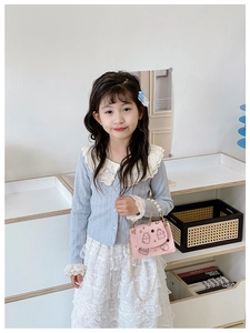 Girl in blue cardigan and lace skirt carrying pink cartoon bag with pearl handle