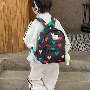 Sac à dos enfant noir à motifs cœurs avec peluche porté par un enfant au dos