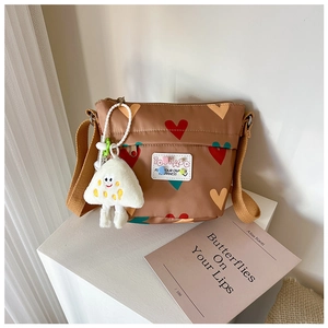 Détail du sac bandoulière marron avec cœurs colorés et pendentif peluche sourire