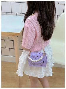 Detail of purple cartoon crossbody bag with pearl handle and golden chain on young model