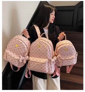 Three sizes of pink backpacks with floral monogram patterns and doll pendant details