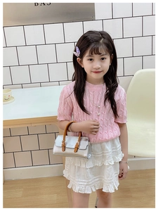 Girl wearing pink knit top and white lace skirt holding a shiny silver handbag