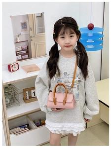 Detail view of pink PU leather child handbag with brown handles in cozy home setting