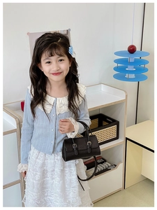 Mini black leather tote for kids with gold buckles shown in a cozy home setting