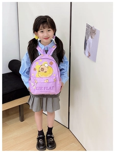 Detail of purple children backpack featuring yellow cartoon character and LIE FLAT print