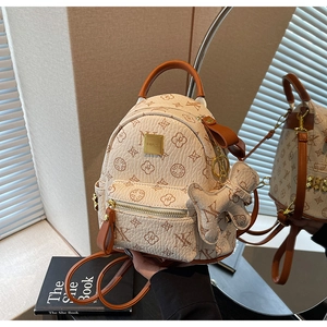Detail of elegant beige mini backpack with vintage monogram print and bear pendant