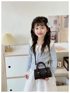 Detail view of mini black pebble grain leather handbag worn by a child model in a home setting