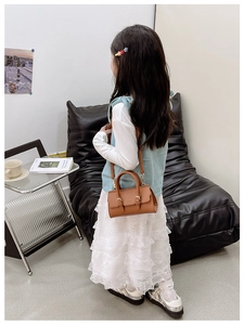 Detailed view of a brown leather toddler crossbody bag with handles and thin shoulder strap