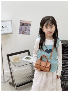 Close-up of brown litchi pattern leather kids handbag with dual buckles and shoulder strap