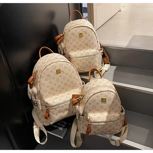 Three sizes of monogrammed backpacks with brown leather trim on a grey stepped display