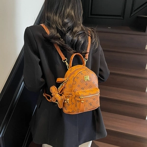 Brown mini backpack with floral monogram pattern and teddy bear charm on stairs