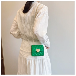 Detail of green quilted mini bag with heart gold clasp and chain strap on a model