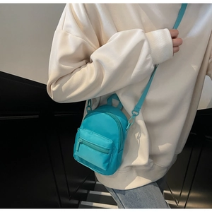 Close-up of vibrant cyan nylon mini crossbody bag shown in use by a model
