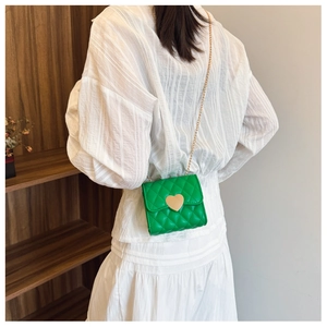 Green quilted mini crossbody bag with gold heart clasp and chain strap on a model