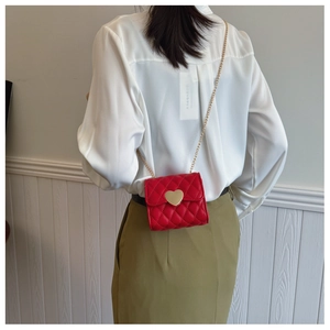 Detail of red quilted mini crossbody bag with gold heart lock and chain strap