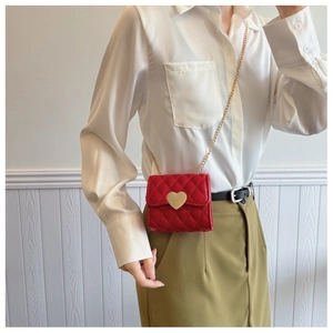 Girl wearing a red quilted mini crossbody bag with a golden heart clasp and chain strap