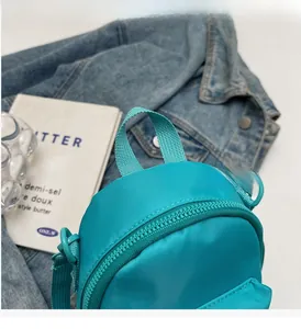 Detail of teal mini crossbody bag with nylon texture and metallic zipper on casual setting