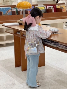 Mini silver mirrored handbag with golden handle shown on a child in a cozy library