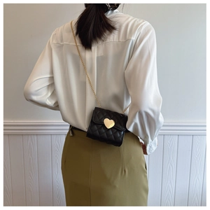 Detail of a mini quilted black crossbody bag with gold heart clasp on a child model