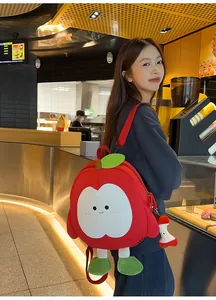 Detailansicht des roten Apfel-Plüschrucksacks mit Cartoon-Gesicht und Apfelkern-Anhänger