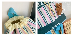 Detail of colorful striped canvas backpack with drawstring closure and plush bear charm