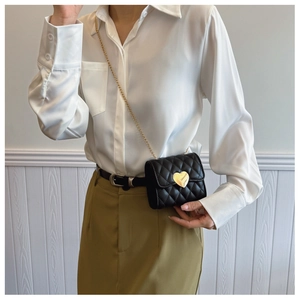 Detail of black quilted mini chain bag featuring a gold heart buckle on a stylish model