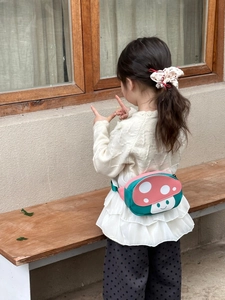 Close-up of cute mushroom-shaped waist bag with green base and pink polka dot cover on a child