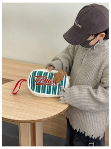 Détail du sac enfant à rayures avec poignée rouge et pendentif ours sur table en bois