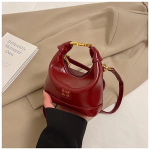 Detailed view of the glossy burgundy leather bag texture with gold metal handle and logo