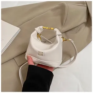 Detail of cream white mini girl's crescent handbag with gold metal bar handle and brand logo