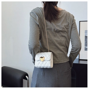 Close-up of white quilted mini crossbody bag with a gold heart clasp and chain strap