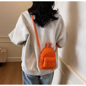 Close-up of a mini orange crossbody bag with adjustable strap worn by a model