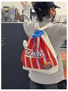 Detail of red and white striped canvas backpack with blue drawstring and teddy bear charm