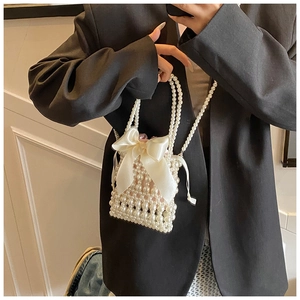 Detailed close-up of a pearl beaded bucket bag featuring a large satin bow and woven handle