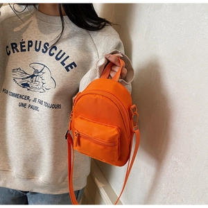 Detailed side view of orange mini crossbody bag with zipper compartments on casual model