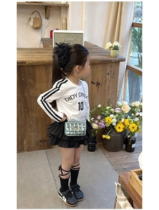 Close-up of a child wearing a stylish green metallic quilted chain bag and skirt