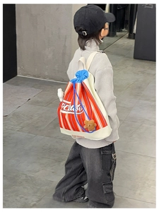 Detail of striped drawstring backpack for kids with cute plush bear charm on a gray outfit