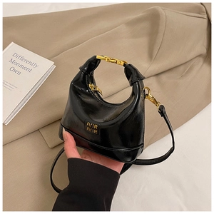 Detail of a mini black glossy leather handbag with gold metal clasp and Arir label
