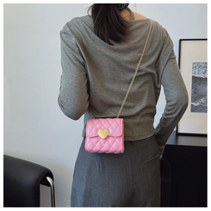 Detailed view of pink quilted leather crossbody bag with gold heart clasp and chain