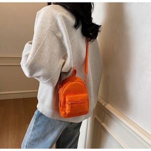 Detail of mini orange crossbody bag with nylon texture and adjustable strap worn by model