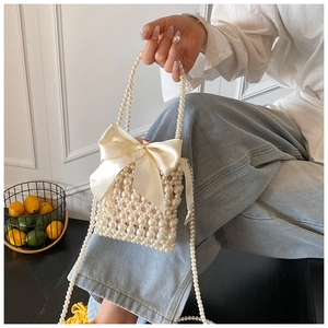Detail of handmade pearl beaded mini bag featuring a large satin bow and woven handle