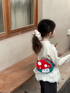 Outdoor shot of a child wearing a cute green mushroom crossbody bag with red polka dots