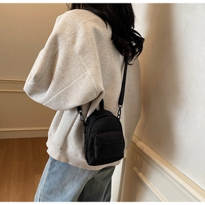 Close-up of the black nylon mini crossbody bag showing zippers and adjustable shoulder strap