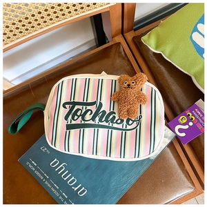 Détail d'une pochette en toile à rayures colorées avec logo vert et ours en peluche