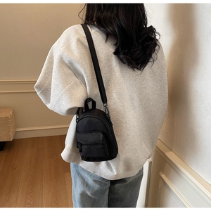 Detailed back view of a compact black nylon crossbody bag worn by a model in a cozy setting