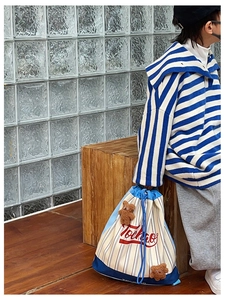 Detail of blue and white striped drawstring backpack featuring brown plush bear charms
