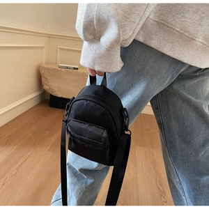 Detail of a mini black nylon crossbody bag featuring a zipper pocket and top handle